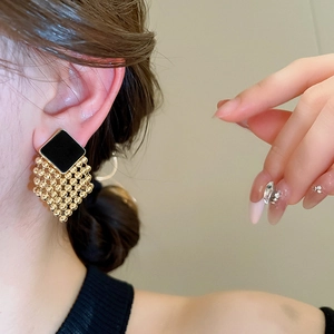 Detail of vintage square black enamel earrings with gold bead tassels on a model