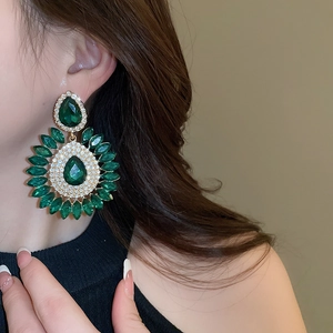 Close-up of emerald green teardrop earrings with crystals worn by a model in social style