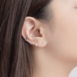 Macro shot of silver cartilage hoop earrings featuring square-cut gemstones in three colors