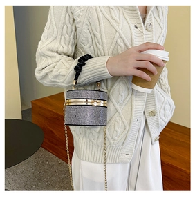 Silver rhinestone cylinder bag with gold metal trim and chain held by a woman