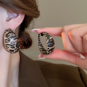 Macro view of C-shaped leopard print faux leather hoop earrings on a model's ear