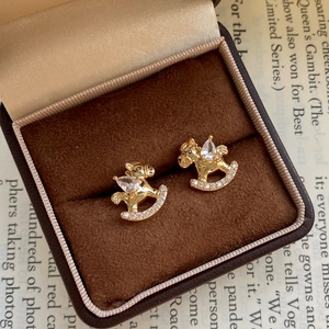Detail of gold-plated rocking horse earrings with cubic zirconia on a velvet display