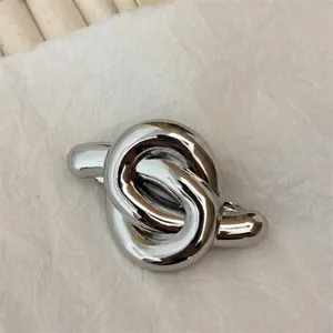 Detail of silver knot hair clip with high-polish finish on neutral textured background