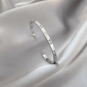 Detail of silver titanium steel bangle featuring hollow Roman numerals and a small zircon