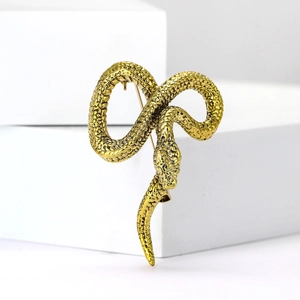 Vintage golden snake brooch with detailed scales on white geometric stand