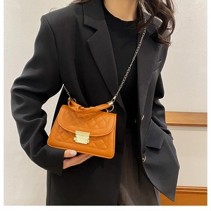 Detalle de bolso acolchado marrón con cadena dorada y cierre sobre blazer negro