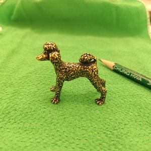 Macro shot of an antique brass poodle figurine with detailed texture next to a pencil