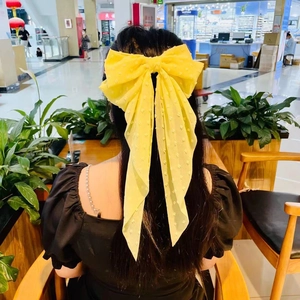 Detail of yellow polka dot oversized bow hair clip worn on long hair from behind