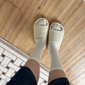 Nahaufnahme beiger Plateausandalen aus EVA mit weißen Socken auf echtem Holzboden