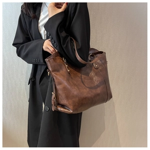 Detail of deep brown leather tote bag with metallic hardware worn with black blazer