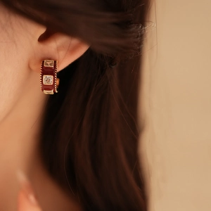 Close-up of vintage C-shaped gold-plated earring with red enamel and square zircon inlay