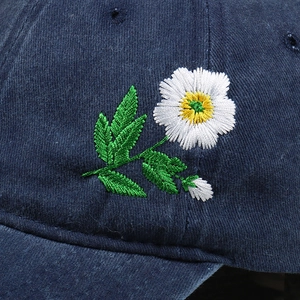 Detailed close-up of navy blue corduroy fabric and delicate floral embroidery on baseball cap