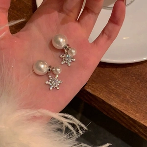 Silver needle snowflake earrings with white pearls and sparkling zircons held in hand