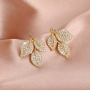 Close-up of golden leaf earrings with shimmering pavé-set zircons on silk fabric