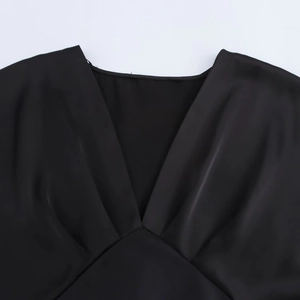 Detail eines schwarzen Satin-Midikleids mit tiefem V-Ausschnitt und drapiertem Stoff