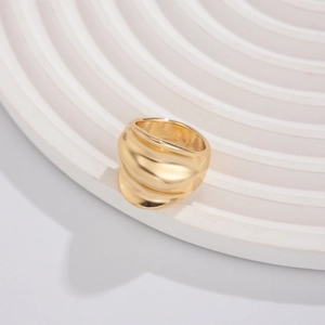 Detailed close-up of wide golden ring with irregular wavy texture on a white tray