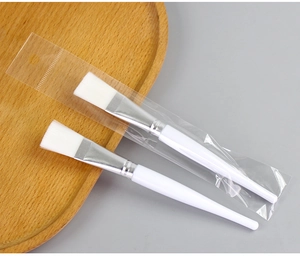 Detail of two white facial mask brushes on wood tray with transparent packaging