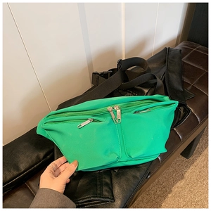 Detail of green nylon crossbody bag with wide black strap and silver zipper pockets