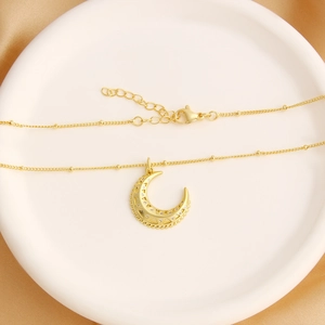 Golden crescent moon necklace with zircon pendant on a bead chain displayed on silk