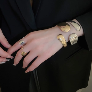 Detailed view of polished gold and silver fluid metal bracelets and rings worn on hand
