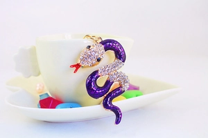 Detailed close-up of purple enamel snake keychain with sparkling rhinestones on a white cup