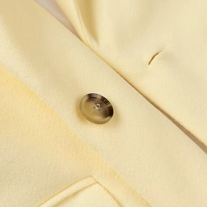 Detailed macro view of yellow wool coat fabric and textured amber button detail