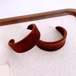 Gros plan de boucles d'oreilles créoles en velours marron foncé sur fond de lin texturé
