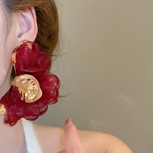 Close-up of red chiffon flower earrings with golden metallic accents on a model