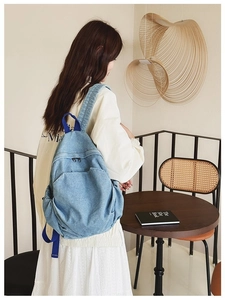 Blue denim backpack shown on a model in a cafe setting for casual lifestyle display