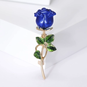 Detailed view of blue rose brooch with green enamel leaves and golden stem on white background