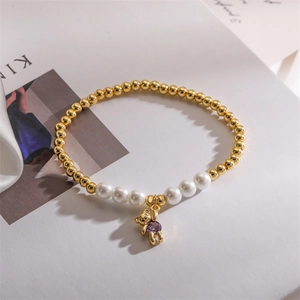 Detailed shot of golden beaded bracelet with pearls and a bear charm with purple zircon