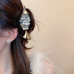 Detailed close-up of a gold-toned fish-shaped hair clip with iridescent shell scales