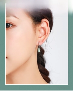 Macro view of sterling silver hoop earrings with a green pave-set dinosaur pendant