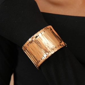 Detailed view of a wide gold metal cuff bracelet with segmented texture on a black sleeve