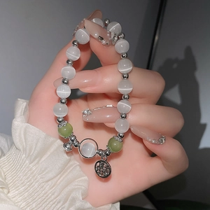 Nahaufnahme von Katzenaugen-Perlenarmband mit silbernem Fu-Anhänger am Handgelenk