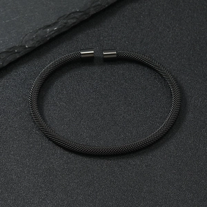 Minimalist matte black stainless steel woven mesh cuff bracelet on dark stone background