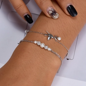 Close-up of double-layer silver bracelet with pearl accents and bird charm on wrist