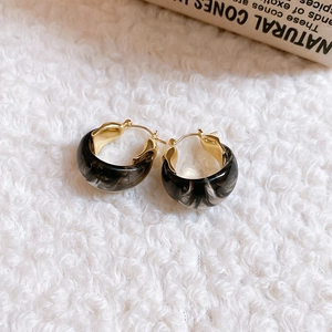 Detail of vintage U-shaped resin earrings with marble texture on white plush background