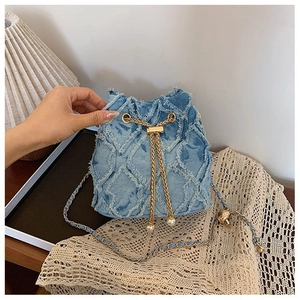 Detail of blue denim bucket bag featuring diamond quilting, fringes, and pearl drawstring