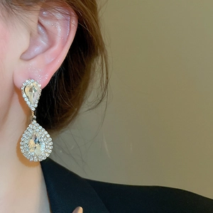 Close-up of elegant gold drop earrings with sparkling rhinestones worn by a model