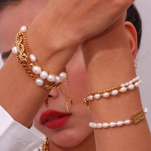 Close-up of layered gold chain bracelet with pearls and 11:11 tag on wrist