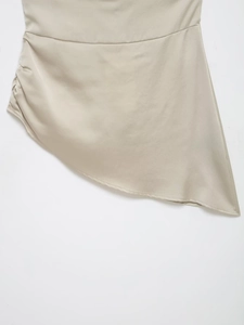 Détails du satin montrant l'ourlet asymétrique et le drapé latéral du haut licou beige