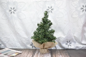 Close-up of a mini green Christmas tree with a natural burlap wrapped base on wood floor
