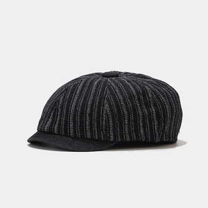 Detail of black newsboy hat with white vertical stripes and top button on white background