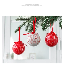 Three red and white Christmas baubles with tree patterns hanging on pine branches