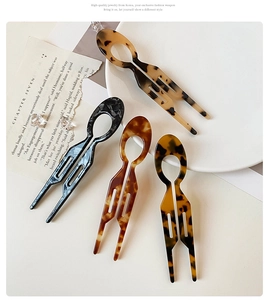 Detail of four acetate hair pins in tortoiseshell and amber patterns on a white tray