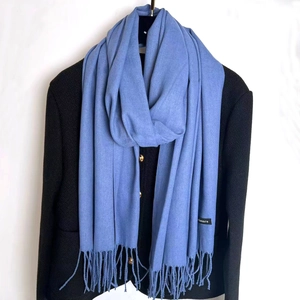 Detailed close-up of light blue cashmere scarf fringes on a dark tweed jacket