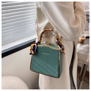 Chic green box bag with silk scarf handle detail shown in a soft sunlit interior