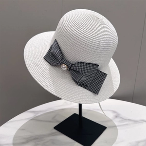 Detail of white straw hat featuring a black and white checkered bow with pearl accent