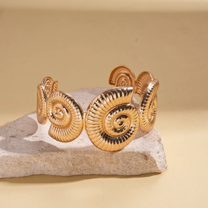 Detail of a gold-plated spiral bangle featuring relief nautilus textures on a grey rock